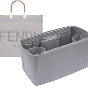 May include: A light gray tote bag with a matching organizer insert. The tote features a rectangular shape with a brown handle and gold accents. The organizer has multiple compartments and a zippered pocket.