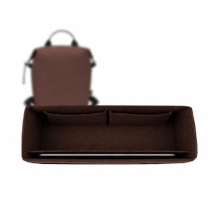 Peut inclure: Un organisateur de sac en feutre marron foncé de forme rectangulaire, doté de plusieurs compartiments et poches intérieurs. L'organisateur est placé au premier plan, tandis qu'un sac à dos marron flou est visible en arrière-plan.