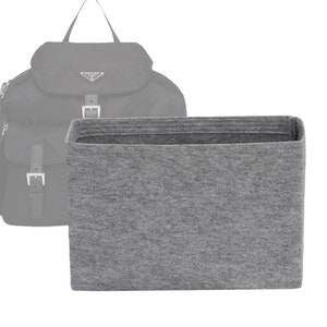 May include: A grey felt bag insert for a backpack. The insert is rectangular and has a smooth, textured surface.