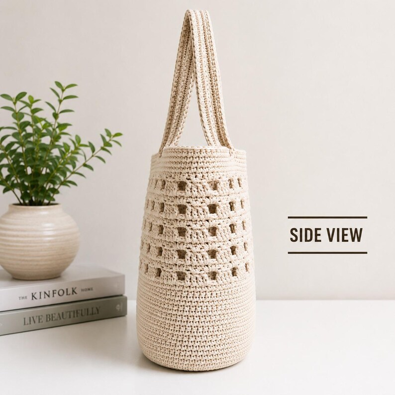 May include: A beige crochet tote bag with a tall, cylindrical shape and a single integrated handle. The bag features a dense, solid base and a middle section with an open, square-patterned weave. The text "SIDE VIEW" is printed to the right.
