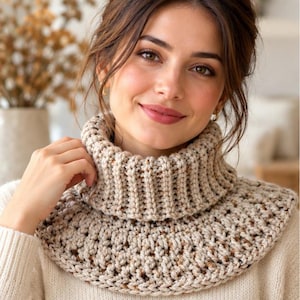 May include: A chunky knit cowl neck warmer in a light beige color with subtle brown and tan flecks throughout. The accessory features a thick ribbed turtleneck collar that transitions into a wider, textured crocheted base that sits on the shoulders.