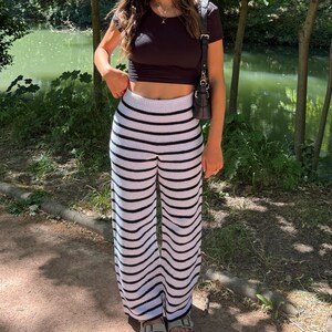 Peut inclure: Un haut court noir à manches courtes associé à un pantalon en tricot taille haute à rayures horizontales noires et blanches. Le pantalon présente une coupe large et une ceinture élastique côtelée pour une tenue décontractée.