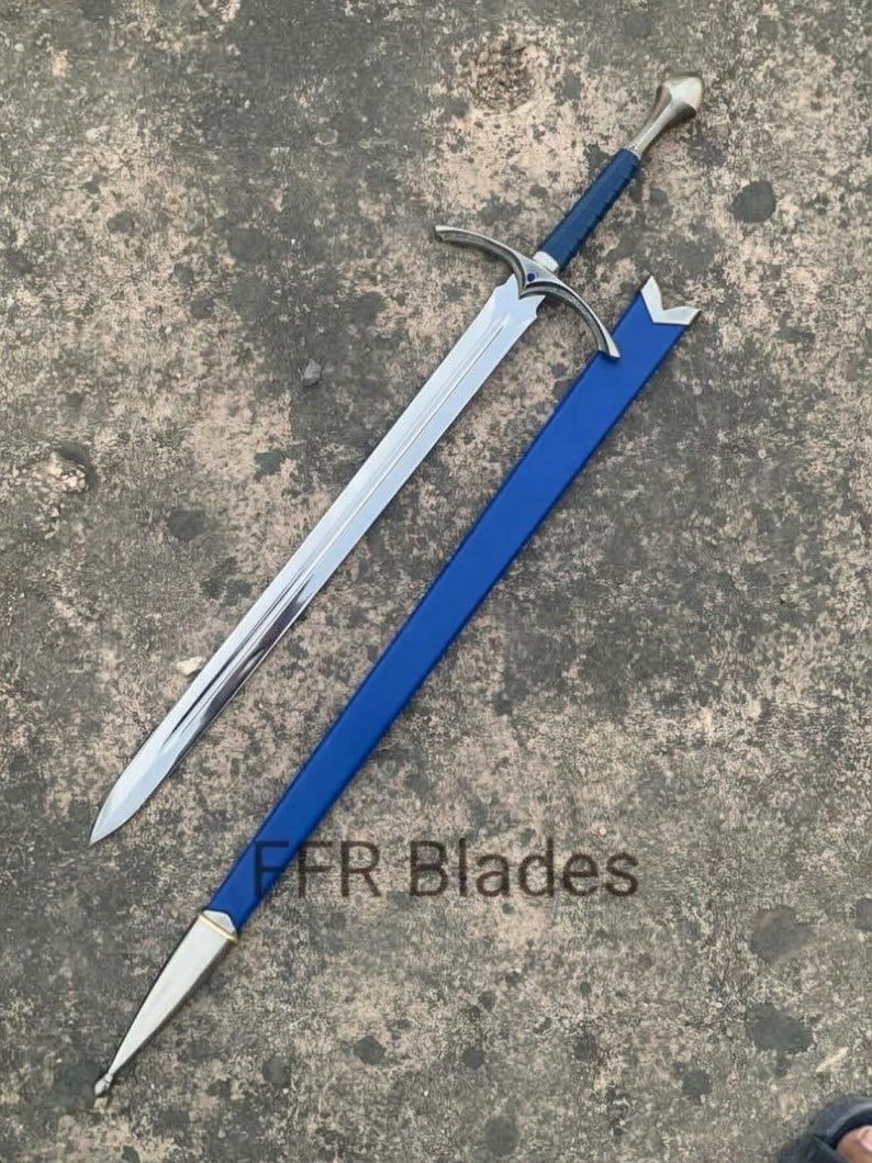 May include: A steel sword with a blue leather-wrapped grip, a silver crossguard, and a matching blue scabbard with silver metal fittings. The text FFR Blades is visible on the scabbard. The blade is double-edged with a central fuller.