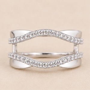 May include: A silver-toned ring guard featuring two parallel, wavy bands connected by vertical bars. Each wavy band is encrusted with a row of small, clear, round-cut stones. The metal has a polished, reflective finish throughout the entire piece.