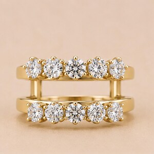 May include: A gold double-band ring featuring two parallel rows of five round-cut clear stones each. The two bands are connected by vertical gold bars on both sides, creating a stacked appearance with ten sparkling stones in total.