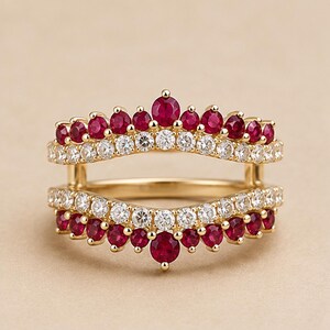 May include: A gold ring guard featuring two curved bands connected by vertical bars. The top band is set with a row of round red rubies and a row of clear white diamonds. The bottom band mirrors this design with clear diamonds and red rubies.