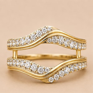 May include: A gold ring guard featuring two curved bands connected by vertical bars. Each band is inlaid with a row of small, clear, round-cut stones that follow the wave-like contour of the metal, creating a symmetrical, open-frame design.