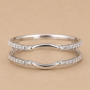 May include: A silver-toned ring guard featuring two parallel bands connected by vertical bars. Each band is encrusted with a row of small, clear, round-cut stones. The center of each band features a smooth, curved arch design in polished metal.