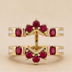 May include: A gold ring guard featuring two bands connected by a vertical bar. The design includes round, deep red rubies set in gold, with small white accent stones embedded along the sides of each band. The structure creates a V-shaped crown.