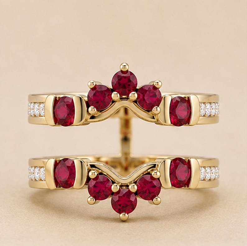May include: A gold ring guard featuring two bands connected by a vertical bar. The design includes round, deep red rubies set in gold, with small white accent stones embedded along the sides of each band. The structure creates a V-shaped crown.