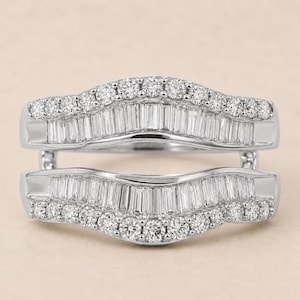 May include: A silver-toned ring guard featuring two curved bands connected at the sides. Each band is set with a row of baguette-cut stones in the center, bordered by a row of small round brilliant-cut stones along the top and bottom edges.