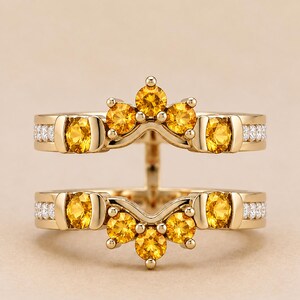 May include: A gold ring guard featuring two bands connected by a vertical bar. The design includes round yellow citrine stones set in a crown-like arrangement and small white diamonds embedded along the sides of the polished gold bands.