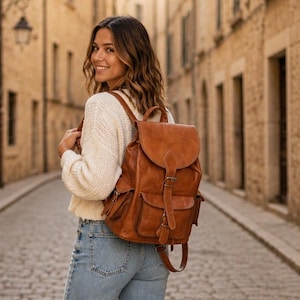 Può includere: Uno zaino in pelle color cuoio con patta ripiegabile e chiusura a fibbia, due tasche laterali e due tasche frontali. Lo zaino è dotato di spallacci regolabili e manico superiore, caratterizzato da una texture liscia e cuciture a vista.