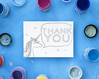 Puede incluir: Una tarjeta de agradecimiento en blanco con un unicornio y estrellas. La tarjeta está rodeada de pequeños recipientes de pintura de varios colores.