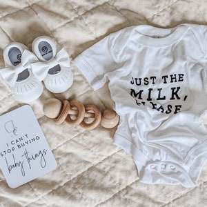 "I can't stop buying baby things" pregnancy milestone card next to baby shoes, rattle and baby onesie