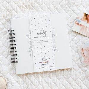Puede incluir: Un diario de embarazo blanco con una encuadernaci&oacute;n en espiral negra. La portada presenta un dise&ntilde;o floral y el texto "The minimalist pregnancy journal 40 weeks of documenting the joys of your journey". La contraportada presenta un logotipo colorido para "nuts & bolts paper co."