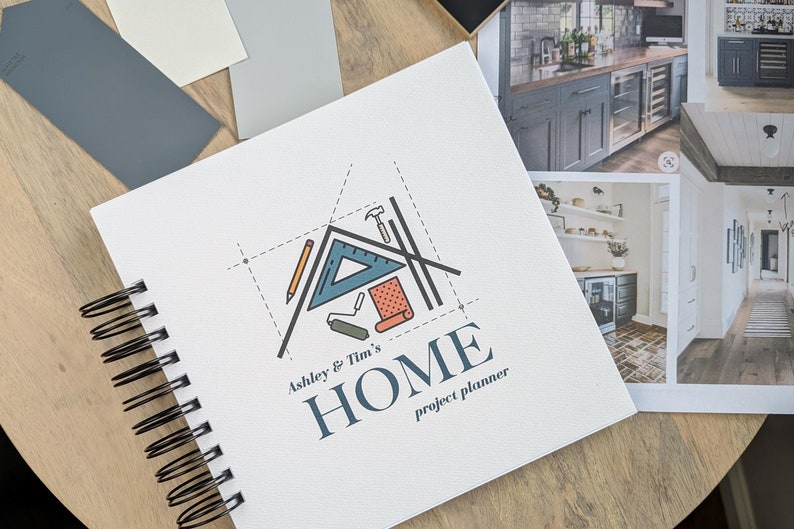 K&ouml;nnte beinhalten: Ein wei&szlig;es Spiralnotizbuch mit einer Haus-Illustration und dem Text "Ashley & Tim's HOME project planner". Das Notizbuch liegt auf einer Holzoberfl&auml;che mit Farbmustern und Inspirationsfotos.