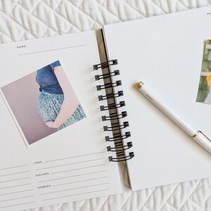 May include: An open white journal with a black spiral binding. The left page has a photo of a pregnant woman and the text "My Mom" with a floral design. The right page has a photo of a mother holding a baby and the text "Photos of Mommy and Me" with a floral design.
