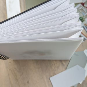 K&ouml;nnte beinhalten: Ein wei&szlig;es Spiralblock mit schwarzem R&uuml;cken. Das Notizbuch ist ge&ouml;ffnet und die Seiten sind aufgef&auml;chert.