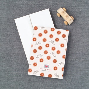May include: A white card with a red and white grapefruit pattern. The card has the text "Nuts & Bolts Paper Co." in black text.