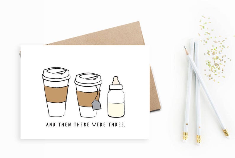 May include: A white card with a black line drawing of two coffee cups and a baby bottle. The text on the card reads "And then there were three."