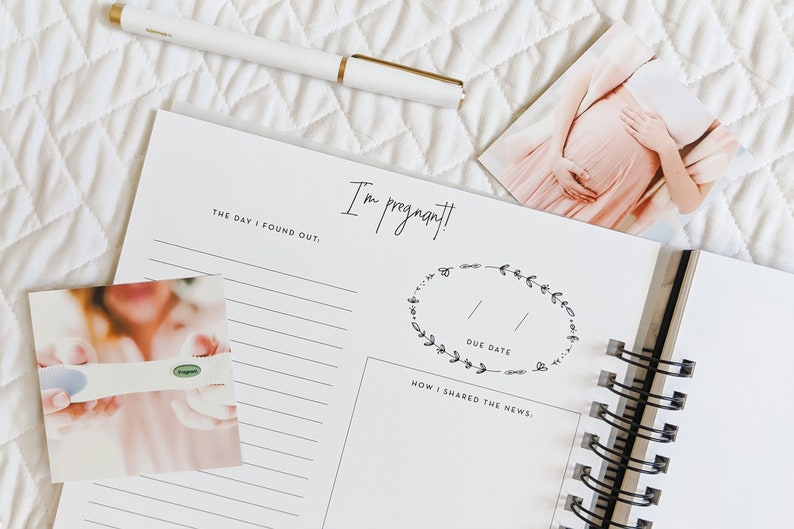 May include: A pregnancy journal with a white cover and black spiral binding. The cover has the text "I'm pregnant!" and a wreath with the words "Due Date". There are two photos on the page, one of a pregnancy test and one of a pregnant woman.