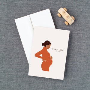 May include: A white card with a simple line drawing of a pregnant person in an orange dress. The text "Thank you" is written in cursive on the card.