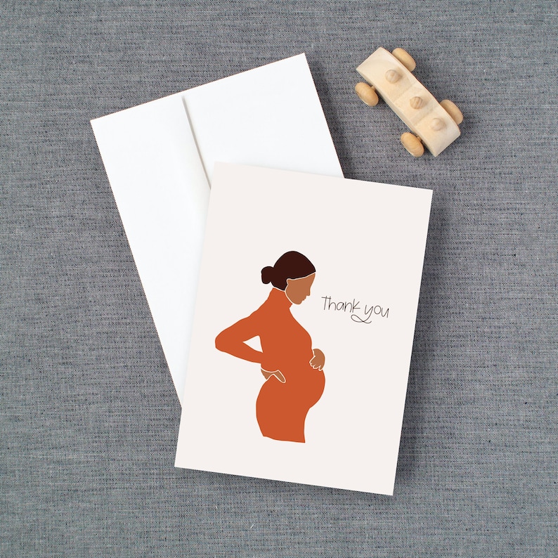 May include: A white card with a simple line drawing of a pregnant person in an orange dress. The text "Thank you" is written in cursive on the card.