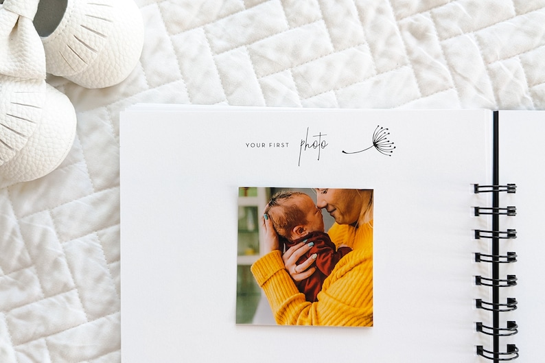 Puede incluir: Un &aacute;lbum de fotos blanco con una encuadernaci&oacute;n en espiral negra. La portada tiene el texto "Your First Photo" y una simple ilustraci&oacute;n de diente de le&oacute;n. Una foto de una madre sosteniendo a un beb&eacute; reci&eacute;n nacido est&aacute; insertada en el &aacute;lbum.