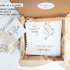 May include: A white box with a brown paper liner, containing a pregnancy journal, a baby book, and a set of milestone cards. The journal has the text "Currently craving" and "Minimalist Pregnancy Journal" on the cover. The box is labeled "Top Seller".