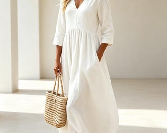 May include: A solid white maxi dress featuring a V-neckline, three-quarter length sleeves, and a gathered waistline that flows into a full-length skirt with side pockets, paired with a woven straw tote bag with two sturdy rope handles.