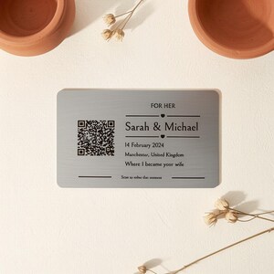 May include: A rectangular gray metal card featuring a black QR code on the left and text on the right that reads FOR HER, Sarah & Michael, 14 February 2024, Manchester, United Kingdom, Where I became your wife, and Scan to relive that moment.