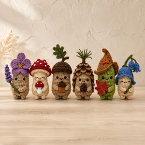 May include: Six small crocheted figures with smiling faces arranged in a row. The figures resemble a purple flower, a red and white mushroom, an acorn with a leaf, a pinecone, a green creature in a brown hat with a leaf, and a blue bell flower.