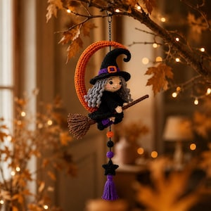 May include: A crocheted hanging ornament featuring a witch with gray hair, a black hat, and a black dress, riding a brown broomstick in front of an orange crescent moon. Below the witch are orange, black, and purple beads, a black star, and a purple tassel.