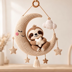 Può includere: Una decorazione da parete all'uncinetto con una mezzaluna beige dal volto addormentato, un bradipo marrone che tiene un cuore bianco, una nuvola bianca e cinque piccole stelle beige. L'oggetto è appeso a un anello di legno con fili di lana.