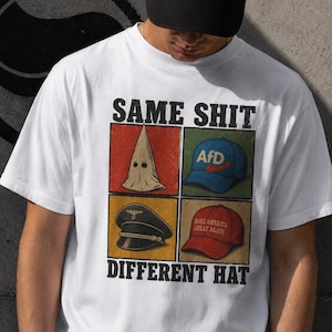 May include: A white t-shirt featuring a graphic print with the text SAME SHIT DIFFERENT HAT. The design includes four squares showing a white pointed hood, a blue AfD baseball cap, a black military-style peaked cap, and a red baseball cap.