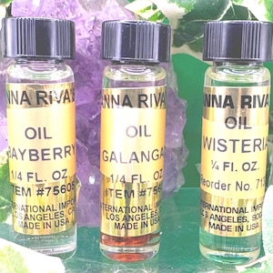 May include: Three small clear glass bottles with black screw-on caps, each containing liquid and featuring a gold label with the text Anna Riva's Oil, specifying the scents Bayberry, Galangal, and Wisteria, with a volume of 7.4 ml per bottle.