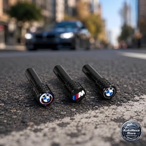 May include: Three black cylindrical valve stem caps with BMW branding. Two caps feature the circular blue and white BMW logo, while the center cap displays the M logo with blue, purple, and red stripes. The caps have a ribbed texture at the top.
