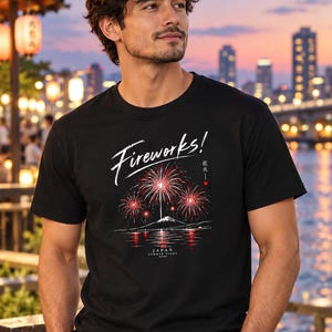 Peut inclure: Un t-shirt noir à manches courtes avec une impression graphique de feux d'artifice rouges au-dessus d'une silhouette de montagne et d'eau. Le texte indique "Fireworks!", "花火" et "JAPAN SUMMER NIGHT" en blanc avec un petit cercle rouge.