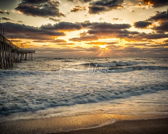 May include: A wooden pier extends out over a sandy beach with foamy waves crashing on the shore. The sun is setting over the ocean, casting golden rays through the clouds.