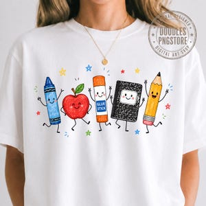 May include: A white t-shirt featuring a colorful graphic of five anthropomorphic school supplies: a blue crayon, a red apple, an orange glue stick labeled GLUE STICK, a black composition notebook, and a yellow pencil, all surrounded by small stars.