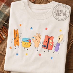 Puede incluir: Una camiseta de color crema con un gr&aacute;fico de cinco personajes antropom&oacute;rficos: una pinza de madera, un recipiente amarillo, una mano, un chaleco rojo y una cuchara morada. Peque&ntilde;as estrellas de colores est&aacute;n dispersas alrededor.