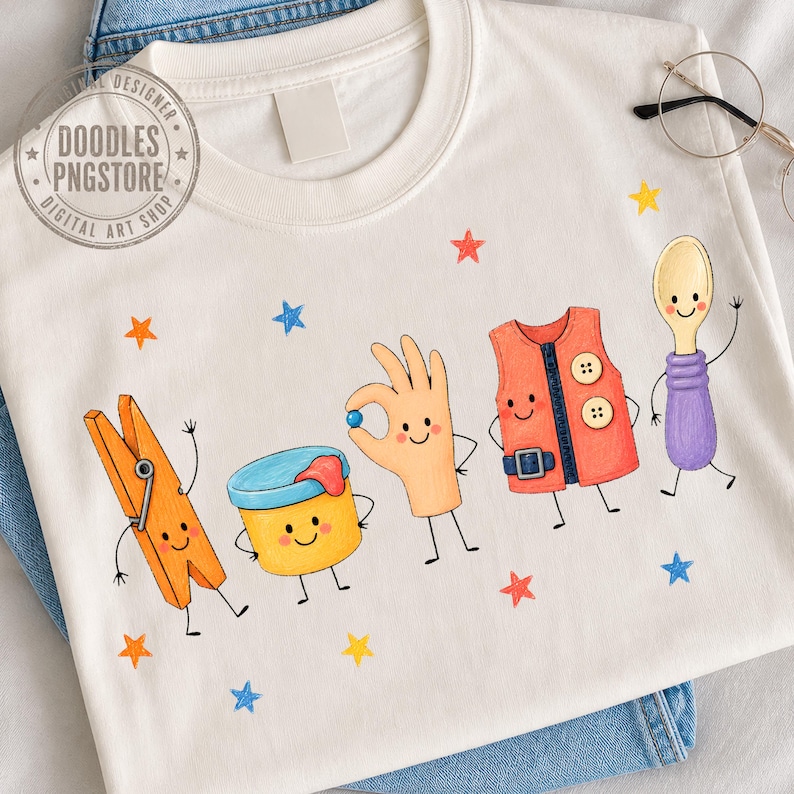 Puede incluir: Una camiseta color crema con un estampado gr&aacute;fico de cinco personajes antropom&oacute;rficos: una pinza de ropa naranja, un recipiente amarillo, una mano beige haciendo un gesto de ok, un chaleco naranja con botones y una cuchara morada, rodeados de estrellas.