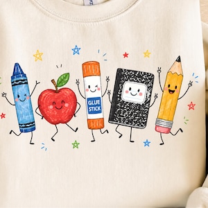 May include: A cream-colored sweatshirt featuring a graphic print of five anthropomorphic school supplies: a blue crayon, a red apple, an orange glue stick labeled GLUE STICK, a black and white composition notebook, and a yellow pencil, surrounded by stars.