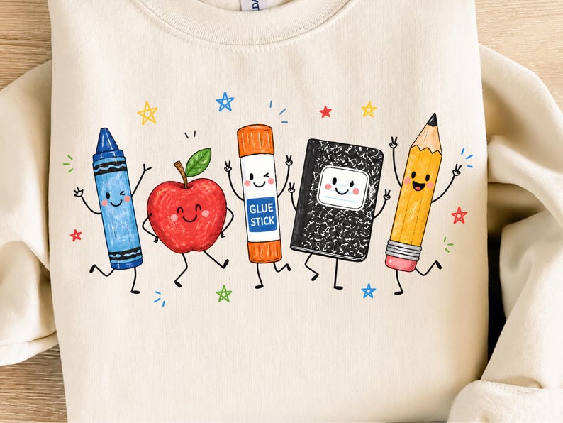 May include: A cream-colored sweatshirt featuring a graphic print of five anthropomorphic school supplies: a blue crayon, a red apple, an orange glue stick labeled GLUE STICK, a black and white composition notebook, and a yellow pencil, surrounded by stars.