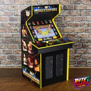 May include: A miniature WWF WrestleFest arcade cabinet featuring a screen displaying a wrestling game, a control panel with four coloured buttons, and side panels decorated with images of professional wrestlers and the WWF logo.
