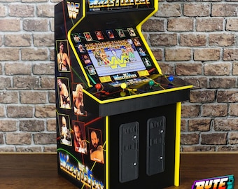 May include: A miniature WWF WrestleFest arcade cabinet featuring a screen displaying a wrestling game, a control panel with four colored buttons, and side panels decorated with images of professional wrestlers and the WWF logo.