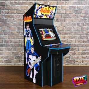 May include: A tabletop arcade cabinet featuring The Punisher branding and character graphics on the side and marquee. The unit includes a screen displaying a video game, a control panel with two blue joysticks, and black casing with blue trim.