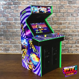 Puede incluir: Una máquina recreativa en miniatura con gráficos de Teenage Mutant Ninja Turtles: Turtles in Time. La unidad presenta un esquema de colores morado y verde, una pantalla que muestra el juego, un panel de control con botones de colores y una marquesina.