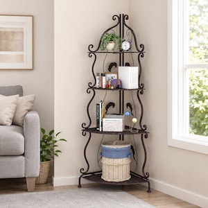 May include: A dark brown metal corner shelf unit with four tiers featuring scrollwork accents. The shelves hold a potted plant, an analog clock, books, small bottles, and a woven basket with a blue fabric lid, all arranged in a corner space.